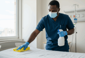 Hospital staff wearing mask and disinfecting patient room and bed.